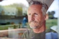 Concerned Senior Man Standing And Looking Out Of Kitchen Door Viewed Through Window