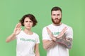 Concerned two friends couple in white volunteer t-shirt isolated on green background. Voluntary free work assistance