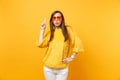 Concerned upset young woman in sweater, heart orange glasses pointing index finger up on copy space isolated on bright Royalty Free Stock Photo