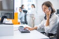 Concerned woman talking on mobile phone, getting bad news and feeling depressed while working on computer at office.