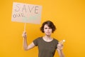 Concerned young protesting girl hold protest sign broadsheet placard on stick, plastic bottle isolated on yellow