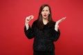 Concerned young woman in black fur sweater spreading hand, holding bitcoin, future currency isolated on bright red