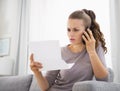 Concerned young woman holding letter and talking mobile phone Royalty Free Stock Photo