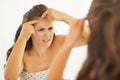 Concerned young woman squeezing acne in bathroom