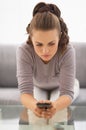 Concerned young woman witn cell phone in hands sitting on couch Royalty Free Stock Photo