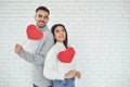 Concert Valentine`s Day. Young couple with hearts in hands on a white brick background