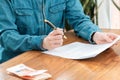 Conclusion of the contract. Close up of woman in a denim shirt holds documents and a pen in her hands. There is money on Royalty Free Stock Photo