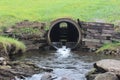 A concrete culvert or tunnel under a grassy bank with timber boards supporting the earth on either side.