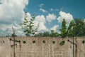 Concrete fence with barbed wire on top against a blue sky with white clouds and green trees. Concept of early release Royalty Free Stock Photo