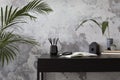 Concrete interior of home office with black desk, image, lamp and office accessories. Grey concrete wall. Home decor. Template