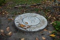 Concrete manhole among the ground, green grass, and fallen autumn leaves Royalty Free Stock Photo