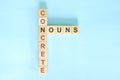 Concrete nouns concept in English grammar noun education. Wooden block crossword puzzle flat lay in blue background. Royalty Free Stock Photo