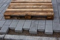 Concrete paver blocks laid beside a building leaving space to the curbstone, a empty wooden pallet is laying on the new paveway