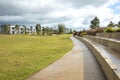 A concrete pedestrian footpath in a park with some modern residential houses or homes in the distance.