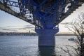 Concrete pillars and steel beams under the Auckland Harbor Bridge illuminated in blue light. A motion blur ferry boat travelling