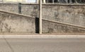 Concrete pole on sidewalk with stairs and railing on a rough cement wall on behind. Street in front. Royalty Free Stock Photo