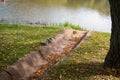 Concrete rainwater gutter, covered with dry fallen leaves on the shore of a pond, reflection, water surface Royalty Free Stock Photo