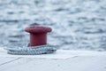 Concrete red mooring bollard with a rope around it at a dock. Royalty Free Stock Photo