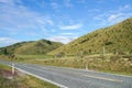 Concrete road along green hill in Lindis Pass New Zealand with clear blue sky Royalty Free Stock Photo