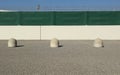 Concrete road bollard in front of a fencing wall made of concrete, plastic tarpaulin and railing.