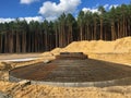 Concrete slab foundation in a forested area in front of a group of pine trees