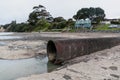 concrete storm water pipe on sea bed at low tide with green park in background