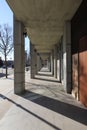 A concrete walkway with stone pillars along the path with bare winter trees and tall black light posts along the street