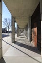 A concrete walkway with stone pillars along the path with bare winter trees and tall black light posts along the street