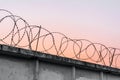 Concrete wall with barbed wire against a blue orange evening sky Royalty Free Stock Photo