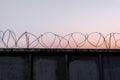 Concrete wall with barbed wire against a blue orange evening sky Royalty Free Stock Photo