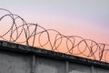 Concrete wall with barbed wire against a blue orange evening sky Royalty Free Stock Photo