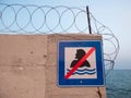 Concrete wall with barbed wire atop and sign Swimming prohibited Royalty Free Stock Photo