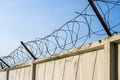 Concrete wall with razor barbed tape wire on blue sky background on a Sunny day Royalty Free Stock Photo