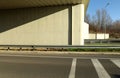 Concrete wall of a road bridge divided in two by shadow . Guard rails , the road below and the exit.