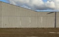 Concrete wall with the top forming an upward angle. Cloudy sky above, sidewalk and asphalt road in front.