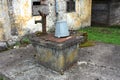 Concrete well with rusted metal cover and grey bucket locked with padlock next to old broken water pump in front of abandoned old Royalty Free Stock Photo