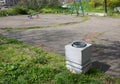 Concrete white trash can on the green grass next to asphalt area of playground in the park.