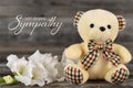 Condolences card with teddy bear and white flower on wooden background Royalty Free Stock Photo