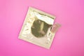 A condom in torn foil pack close up on pink background