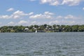 Condos beside the lake among the trees under a cloudy blule sky with a sailboat and a pontoon out on the water