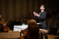 Conductor of symphony orchestra with performers in background in concert hall