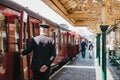 Conductor in uniform closing a door of retro Poppy Line steam train at Sheringham station, Norfolk, UK