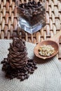 Cone, pine nuts in the glass and shelled nuts in the wooden spon on the braided surface.