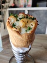 A cone pizza with white pasta stuffed with cheese , coriander leaves on it ,with spices served on it