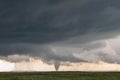 A cone tornado touches down under the base of a dark storm on the plains. Royalty Free Stock Photo