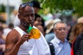 Coney Islands annual mermaid parade, an african man stands in a crowd and drinks a refreshing drink, Brooklyn, New York City, USA