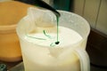 Confectioner in chef uniform is adding mint essence with spatula. Woman adds a mint extract and a concentrate to ice cream.