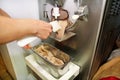 Confectioner in chef uniform is working on ice cream maker machine. Woman is producing ice cream of hazelnut flavors.