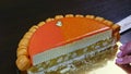 Confectioner by knife tries to take half of orange glazed cheesecake on interlayer
