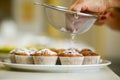 Confectioner sprinkles freshly baked muffins with icing sugar. Sweet pastries, recipes, cooking Royalty Free Stock Photo